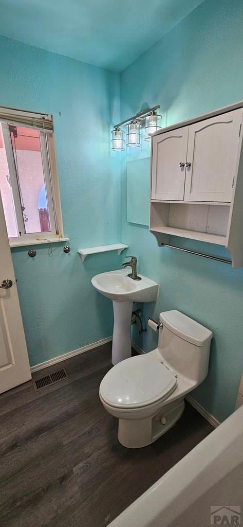 bathroom with visible vents, baseboards, toilet, wood finished floors, and a sink