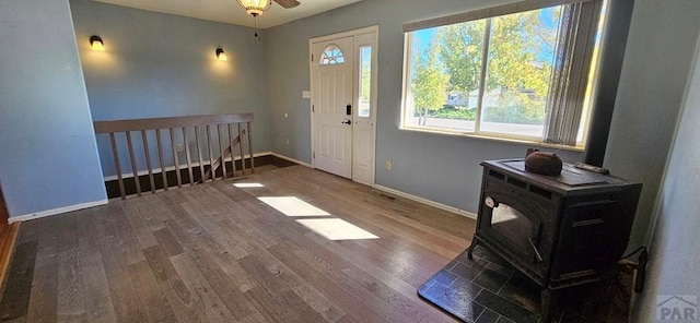 entrance foyer featuring ceiling fan, wood finished floors, a wood stove, and baseboards