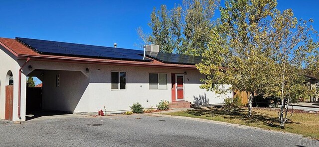 ranch-style house featuring entry steps, roof mounted solar panels, and stucco siding