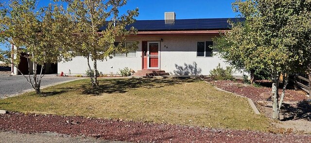 single story home with entry steps, roof mounted solar panels, and a front lawn