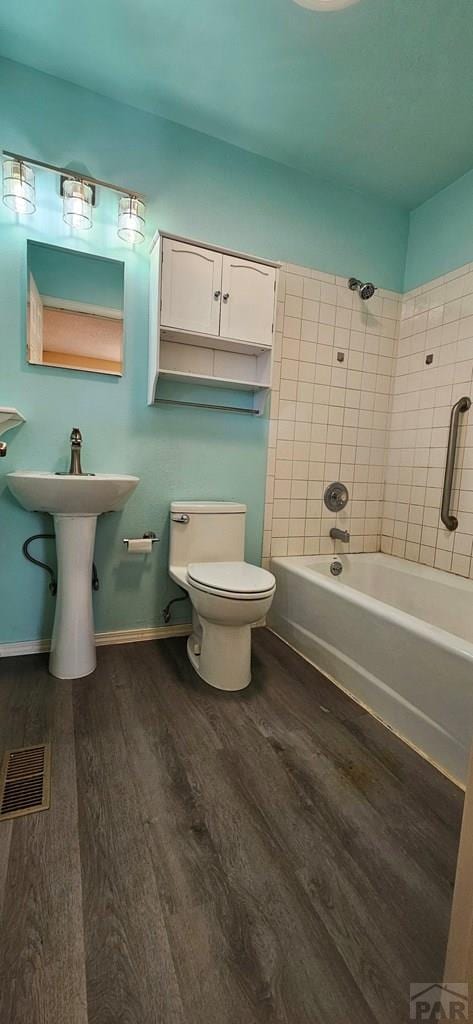 bathroom featuring toilet, wood finished floors, visible vents, baseboards, and washtub / shower combination