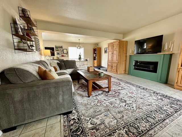 living room with light tile patterned flooring, a glass covered fireplace, and an inviting chandelier