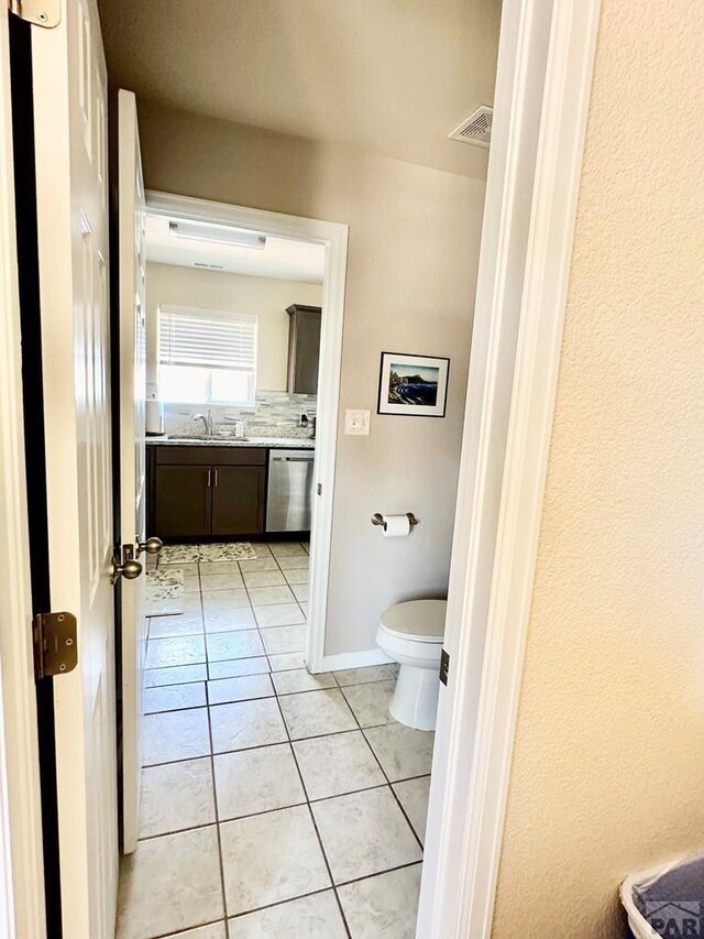 bathroom featuring toilet, a sink, visible vents, backsplash, and tile patterned floors