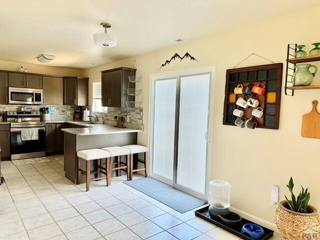 kitchen with a peninsula, a sink, stainless steel appliances, a kitchen bar, and backsplash