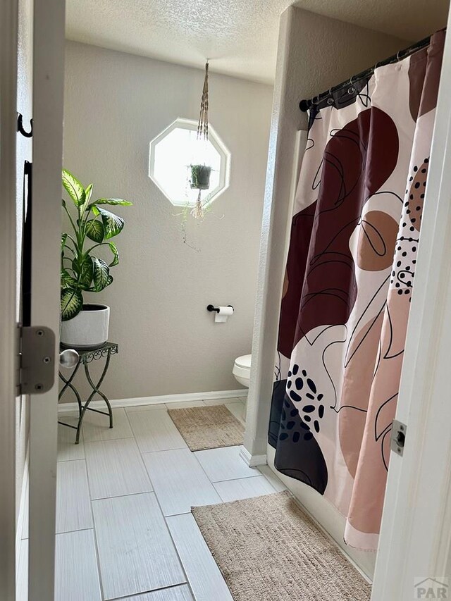 bathroom featuring a textured ceiling, a textured wall, toilet, and baseboards