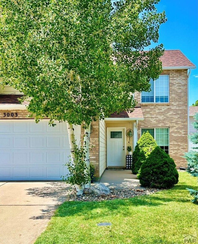 view of front of house featuring a garage, brick siding, a shingled roof, concrete driveway, and a front lawn