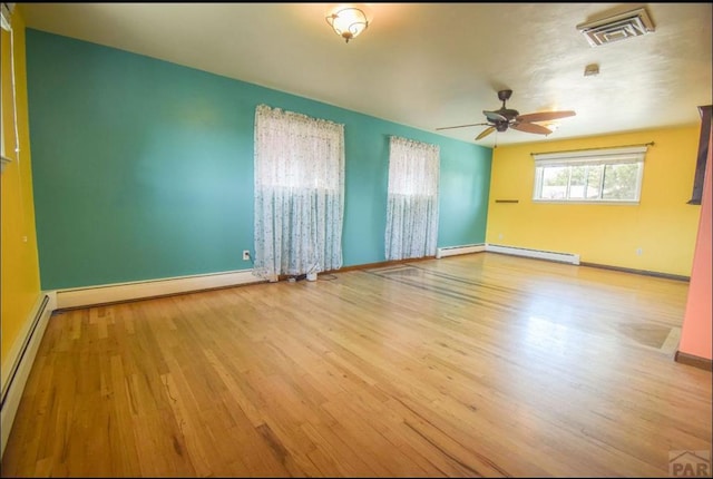 empty room with a baseboard heating unit, wood finished floors, visible vents, baseboards, and baseboard heating