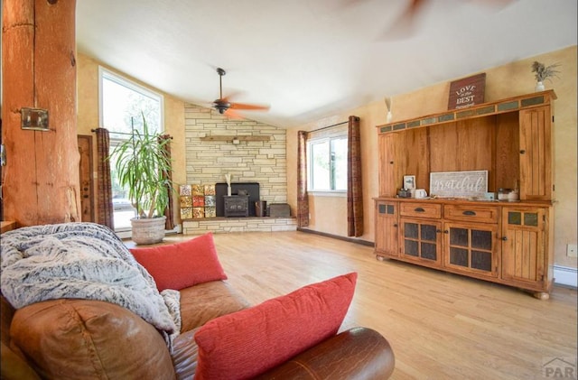 living room with a ceiling fan, a baseboard heating unit, a wood stove, vaulted ceiling, and wood finished floors