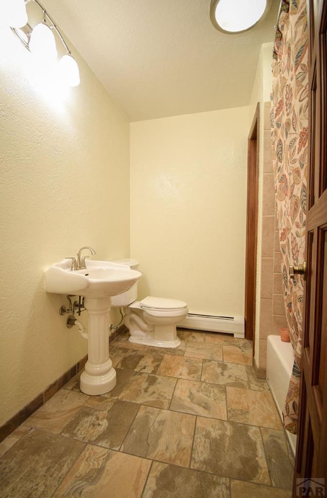 full bathroom with toilet, a baseboard radiator, stone tile flooring, and baseboards