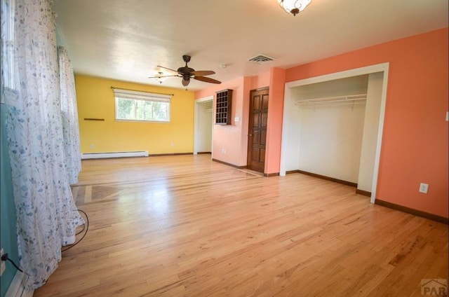 unfurnished bedroom featuring light wood-style flooring, baseboard heating, visible vents, and multiple closets