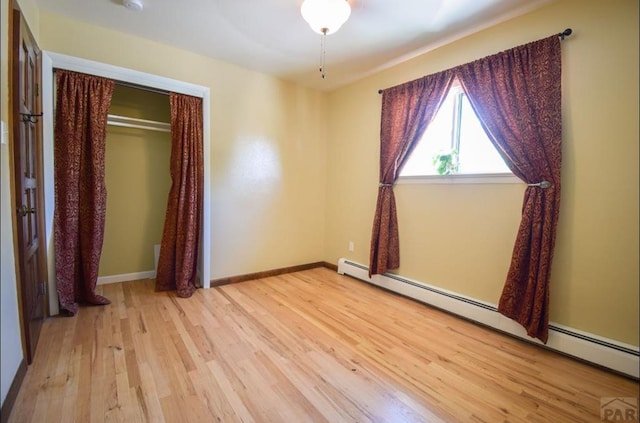 unfurnished room with baseboards, a baseboard heating unit, and wood finished floors