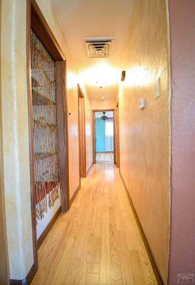 hall with light wood-style floors, visible vents, and baseboards