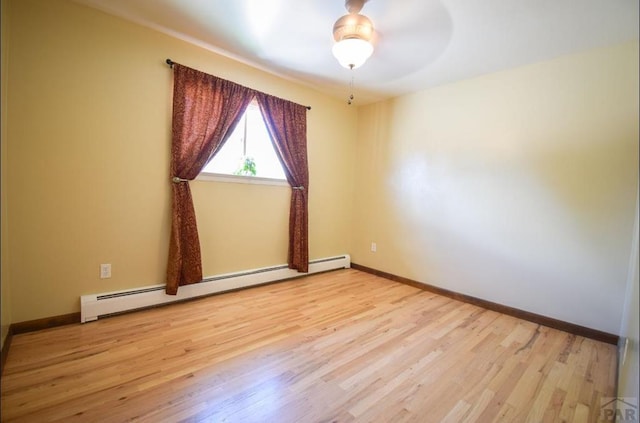 spare room with a baseboard heating unit, wood finished floors, and baseboards