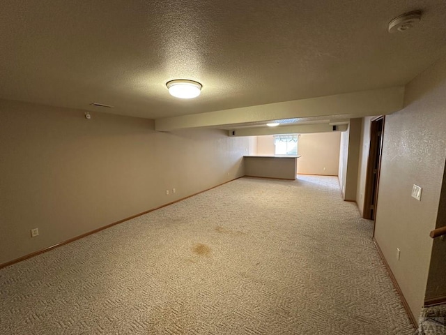 basement featuring light colored carpet, baseboards, and a textured ceiling