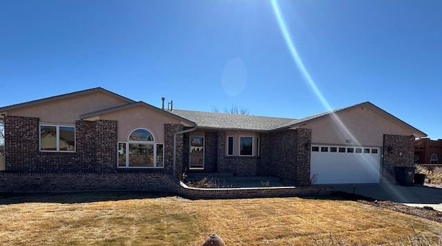 single story home with brick siding, concrete driveway, a front yard, stucco siding, and an attached garage