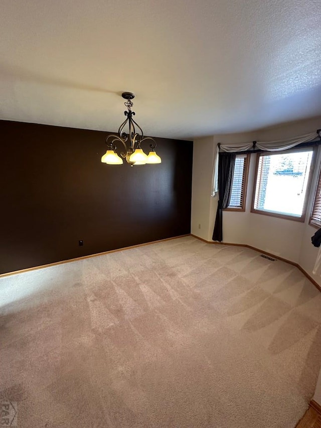 spare room featuring an inviting chandelier, light colored carpet, baseboards, and visible vents