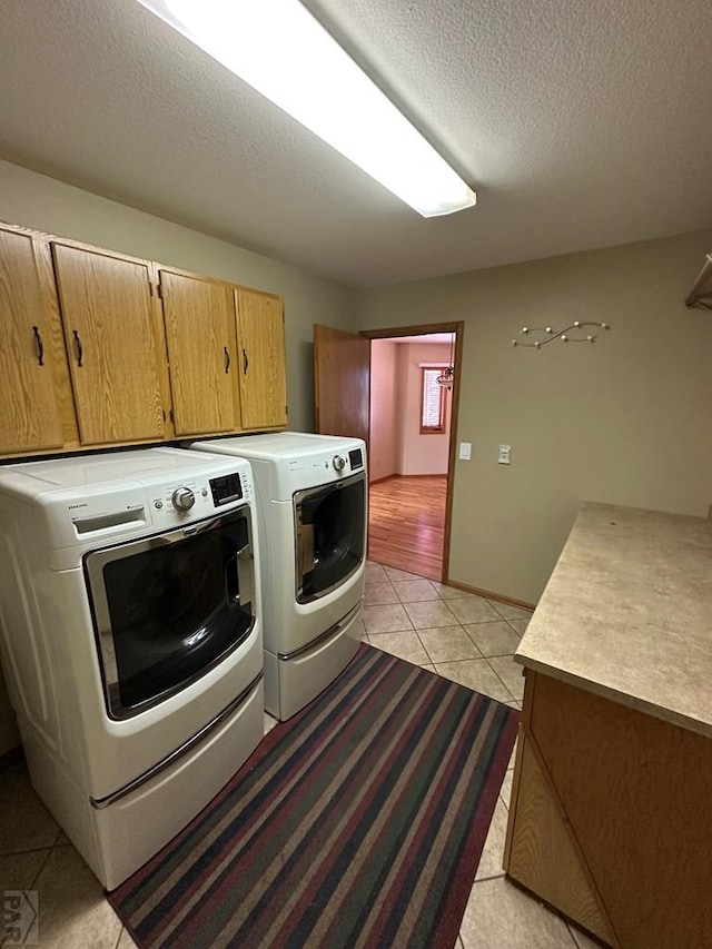 laundry room featuring baseboards, light tile patterned flooring, cabinet space, a textured ceiling, and washing machine and dryer