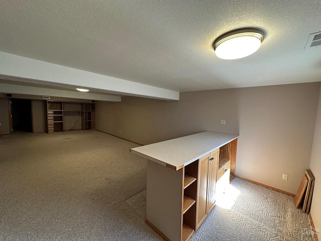 finished below grade area featuring light carpet, visible vents, a textured ceiling, and baseboards