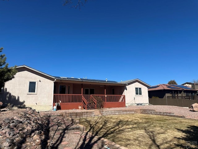 rear view of house with fence, covered porch, and stucco siding