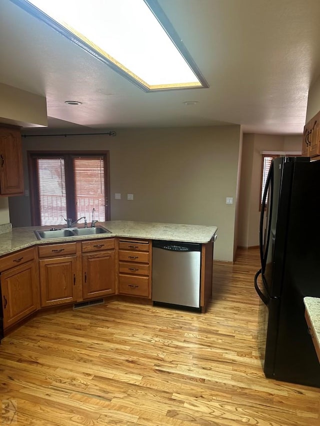 kitchen with a sink, freestanding refrigerator, light wood finished floors, dishwasher, and light countertops