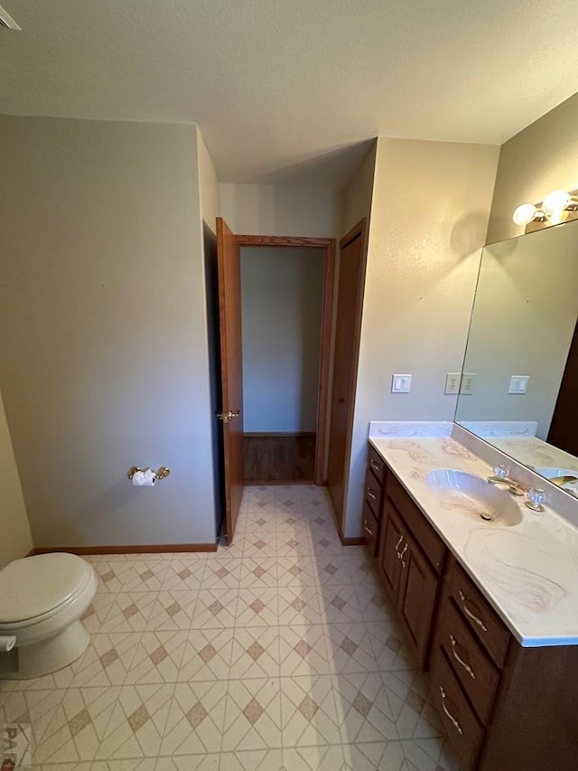 half bathroom featuring tile patterned floors, baseboards, toilet, and vanity