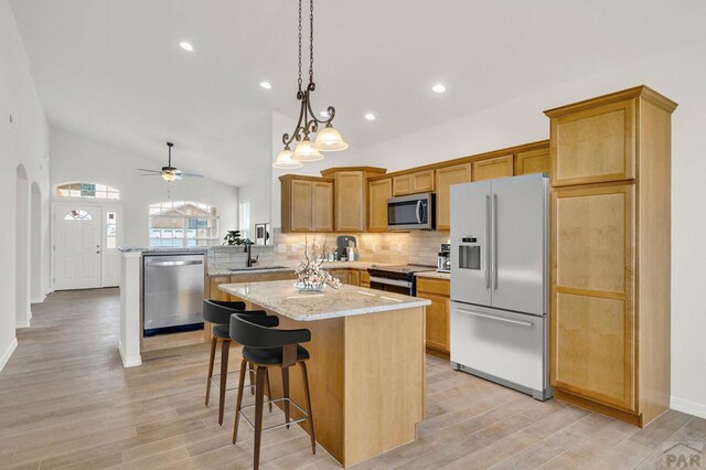 kitchen featuring arched walkways, a sink, a center island, appliances with stainless steel finishes, and decorative backsplash