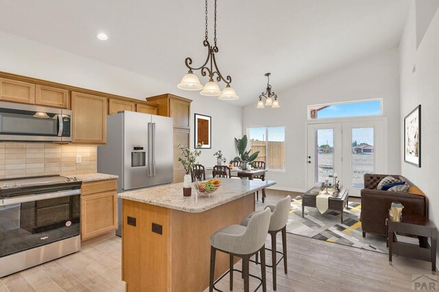 kitchen featuring light wood finished floors, appliances with stainless steel finishes, open floor plan, a center island, and hanging light fixtures