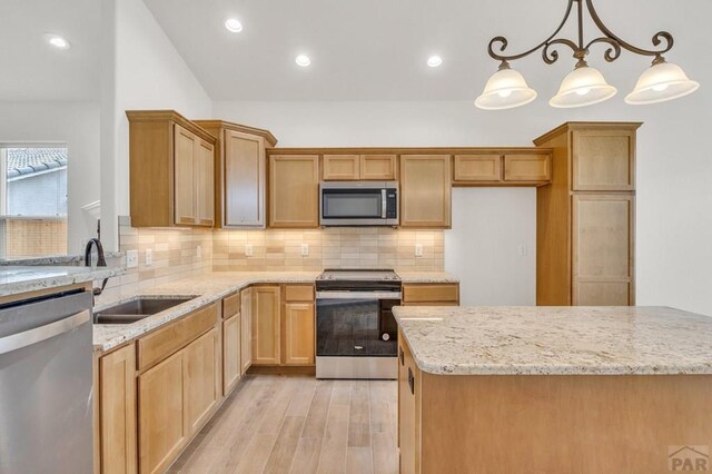 kitchen featuring light stone counters, stainless steel appliances, a sink, hanging light fixtures, and light wood-type flooring