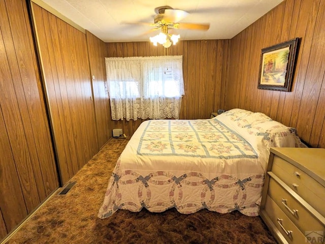 bedroom with wooden walls, visible vents, dark colored carpet, and a ceiling fan