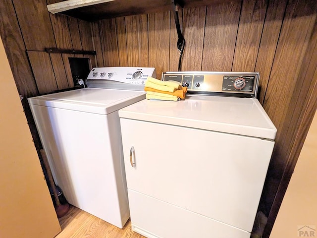 laundry area with light wood-style floors, wooden walls, laundry area, and separate washer and dryer