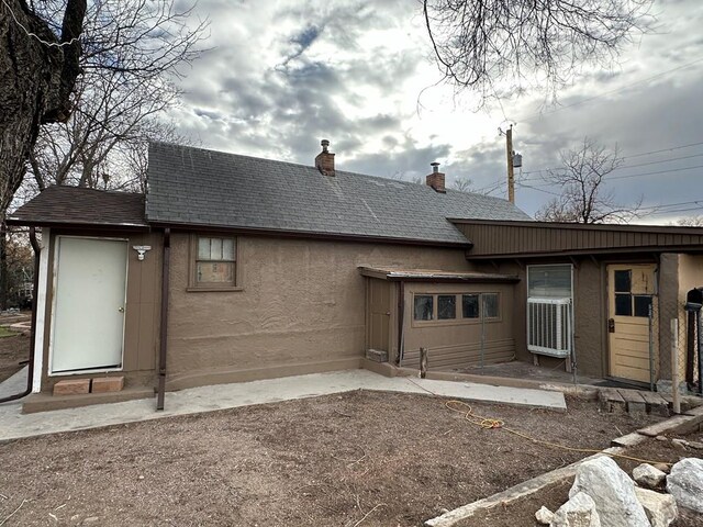 back of house featuring roof with shingles, a chimney, and stucco siding