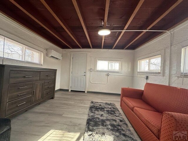 living room featuring light wood-style floors, a wall unit AC, a textured wall, and baseboards