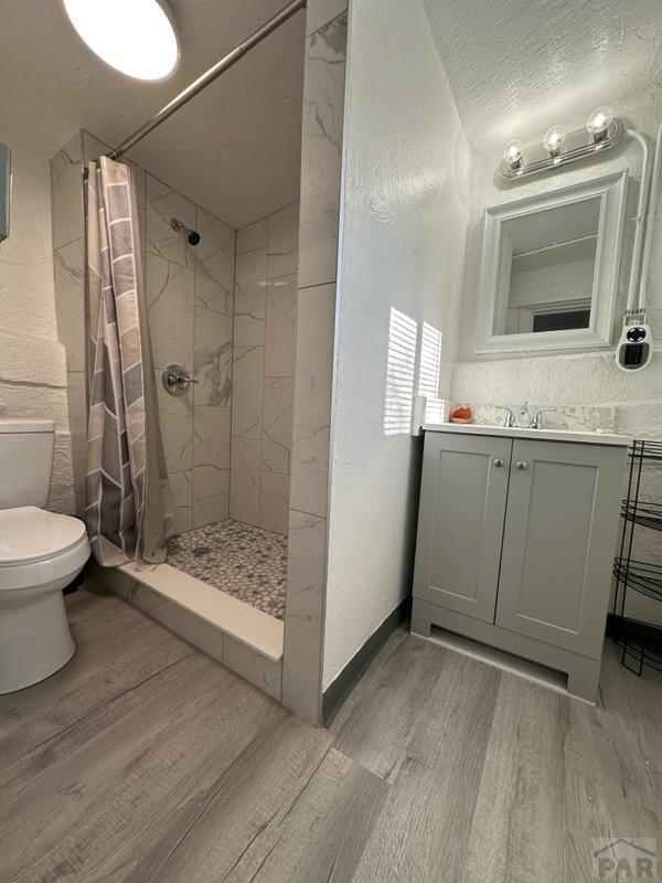 bathroom with toilet, vanity, a shower stall, wood finished floors, and baseboards