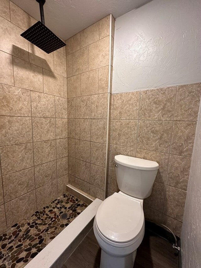 bathroom featuring a stall shower, wood finished floors, toilet, and tile walls