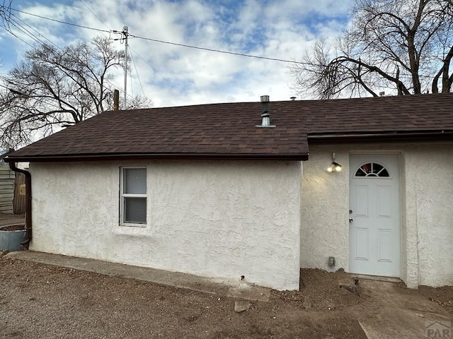 exterior space featuring a shingled roof and stucco siding