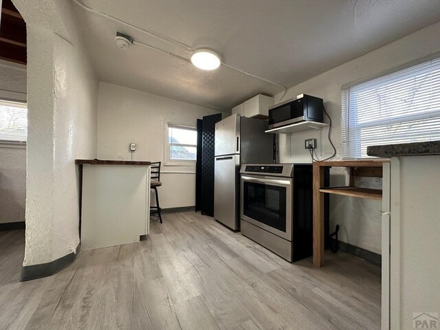 kitchen with dark countertops, appliances with stainless steel finishes, light wood-style floors, white cabinetry, and baseboards