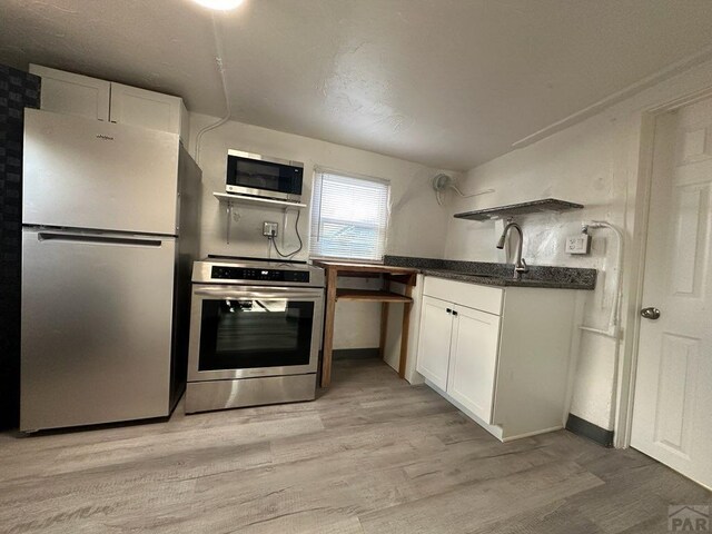 kitchen with white cabinets, dark countertops, light wood-type flooring, and stainless steel appliances