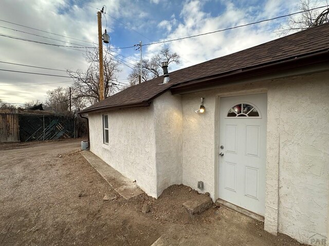 view of exterior entry with a shingled roof and stucco siding