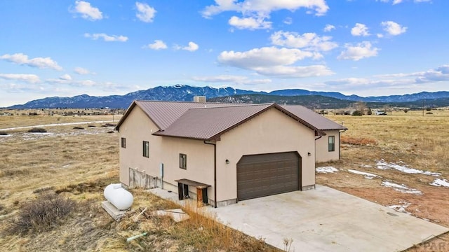 view of home's exterior with stucco siding, an attached garage, metal roof, a mountain view, and driveway