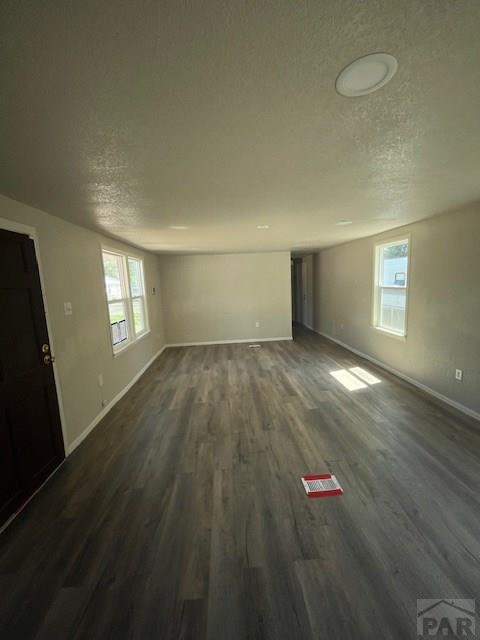 unfurnished living room featuring a textured ceiling, baseboards, and dark wood-style flooring