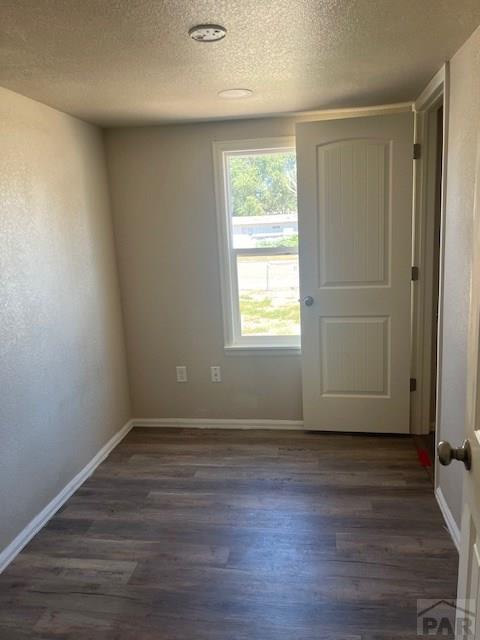 unfurnished room featuring dark wood finished floors, a textured ceiling, and baseboards