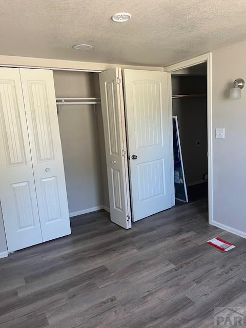 unfurnished bedroom featuring dark wood-style floors, a textured ceiling, baseboards, and a closet