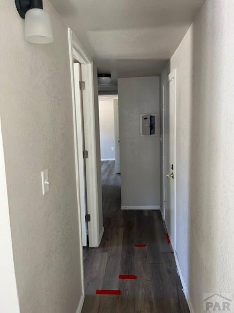 corridor with a textured wall, dark wood-type flooring, and baseboards