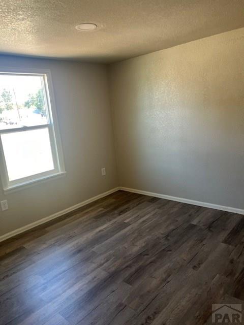 empty room with a textured ceiling, dark wood-style flooring, and baseboards