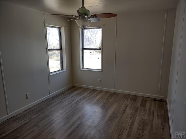 spare room with ceiling fan, visible vents, baseboards, and dark wood-type flooring