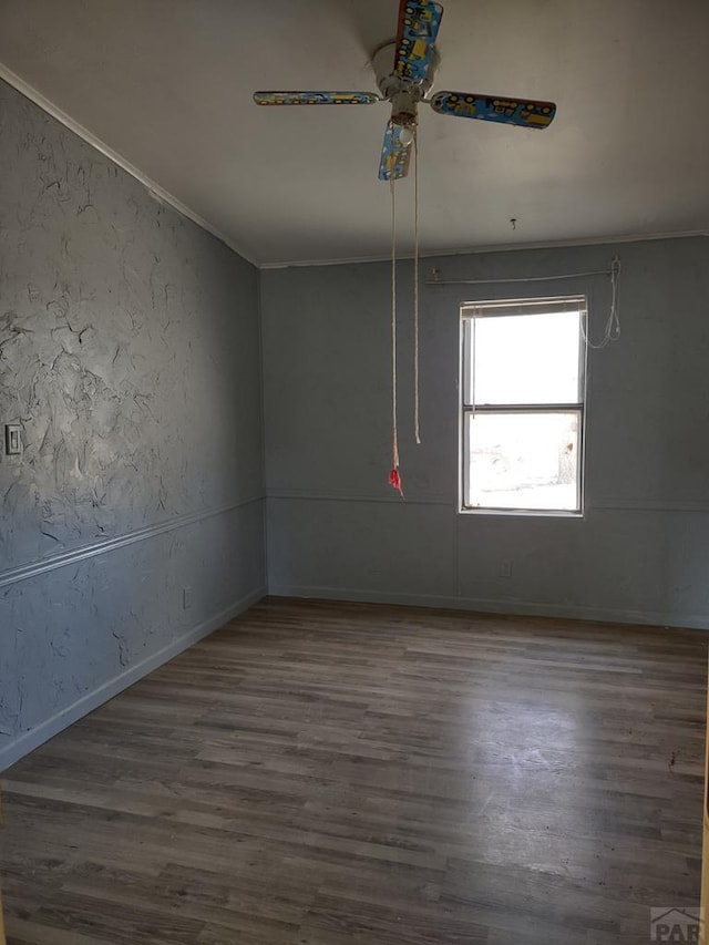 spare room featuring dark wood-style floors, a textured wall, ornamental molding, ceiling fan, and baseboards