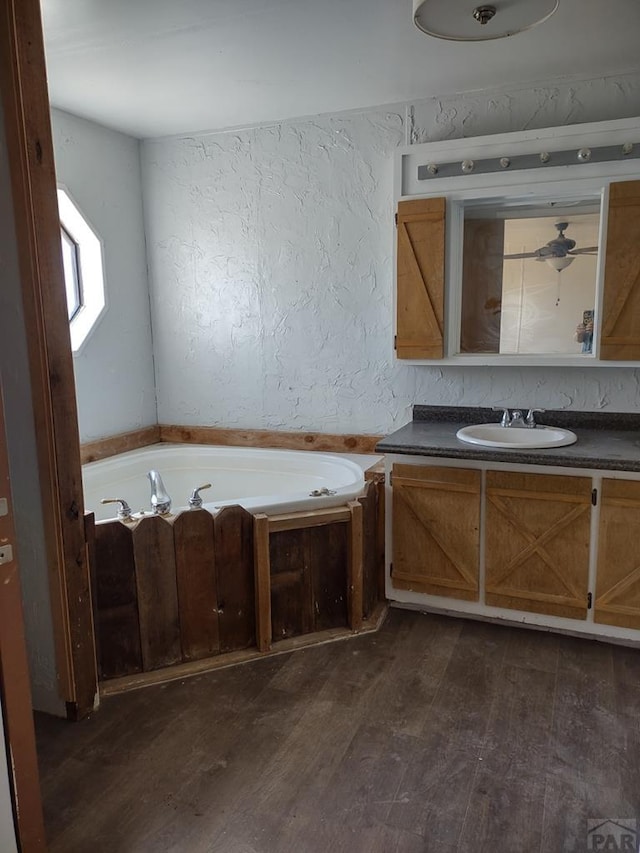 full bath featuring a bath, vanity, wood finished floors, and a textured wall