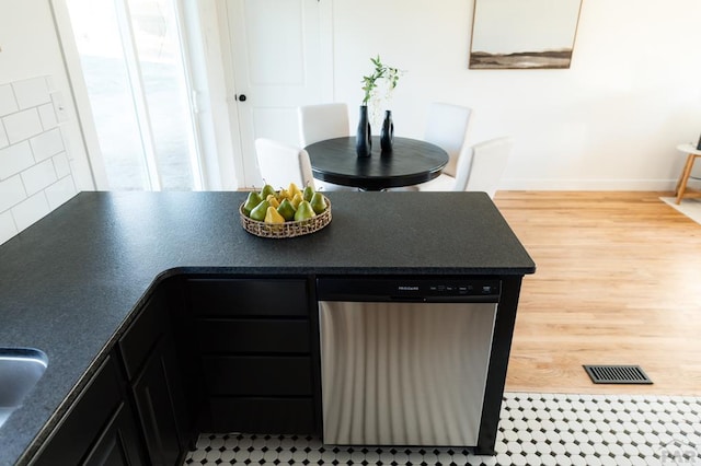 kitchen with light wood-style flooring, visible vents, baseboards, stainless steel dishwasher, and dark countertops