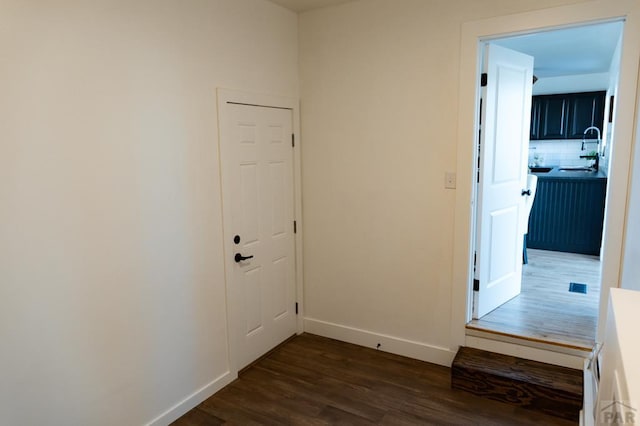 hall featuring dark wood-style floors, a sink, and baseboards