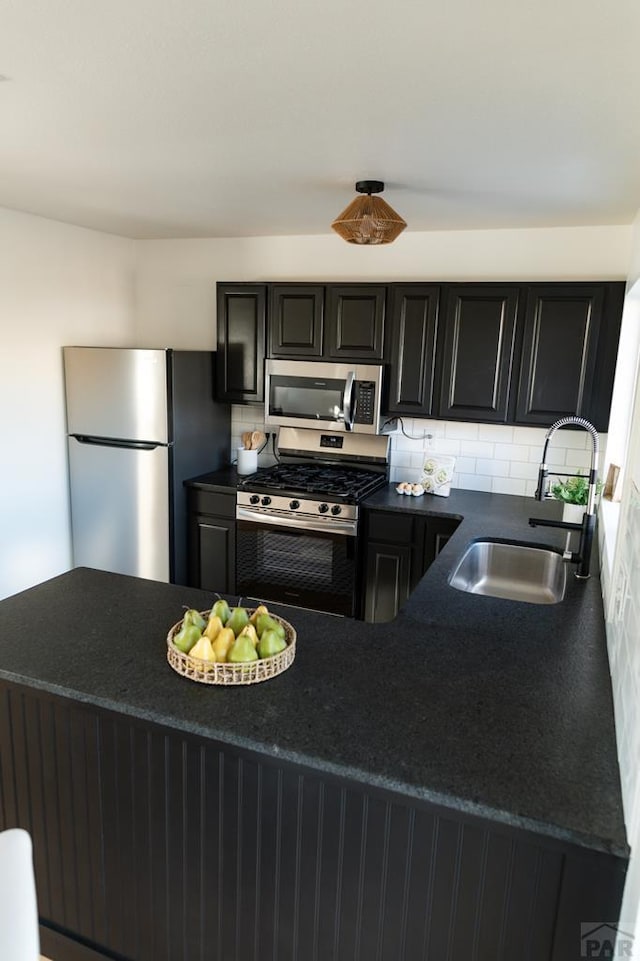 kitchen featuring dark countertops, appliances with stainless steel finishes, a sink, dark cabinetry, and backsplash